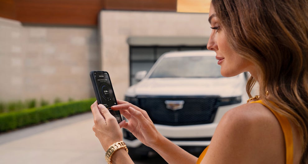 lady checking her mobile with a Cadillac vehicle background | Paul Conte Cadillac in Freeport NY